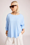 Woman wearing a light blue Eb & Ive  top and white pants with sunglasses on a plain background
