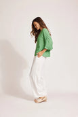 Woman wearing a green Eb & ive top and white pants on a plain background