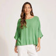 Woman wearing a green Eb & Ive top and white pants on a plain background
