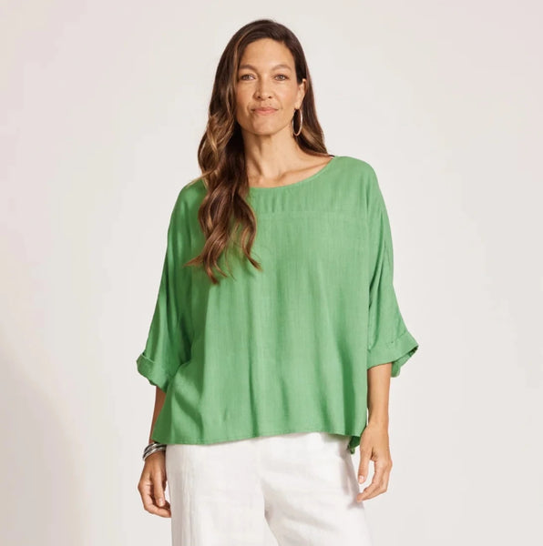 Woman wearing a green Eb & Ive top and white pants on a plain background