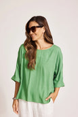 Woman wearing a green Eb & Ive blouse and sunglasses on a plain background