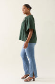 Woman wearing a green isle of mine  top and blue jeans on a white background