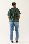 Person wearing a green isle of mine  top and blue jeans on a white background