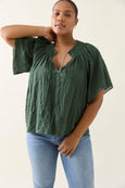 Woman wearing a green isle of mine blouse and blue jeans against a plain background