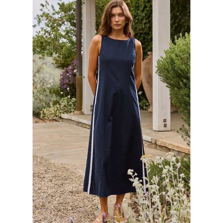 Woman wearing a navy blue dress standing outdoors with greenery in the background