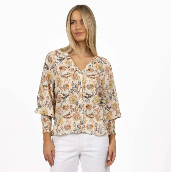 Woman wearing a floral blouse and white pants on a white background