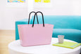 Pink tote bag with black handles on a white table against a blue couch background
