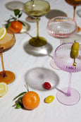 Cocktail glasses with colorful rims and garnishes on a white surface with fruits.