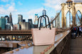 Pink tote bag with black handles on a bridge with a city skyline in the background