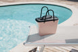 Pink tote bag with black handles on a lounge chair by a pool