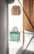 Green bag on a small shelf against a wooden wall with a woven light fixture.