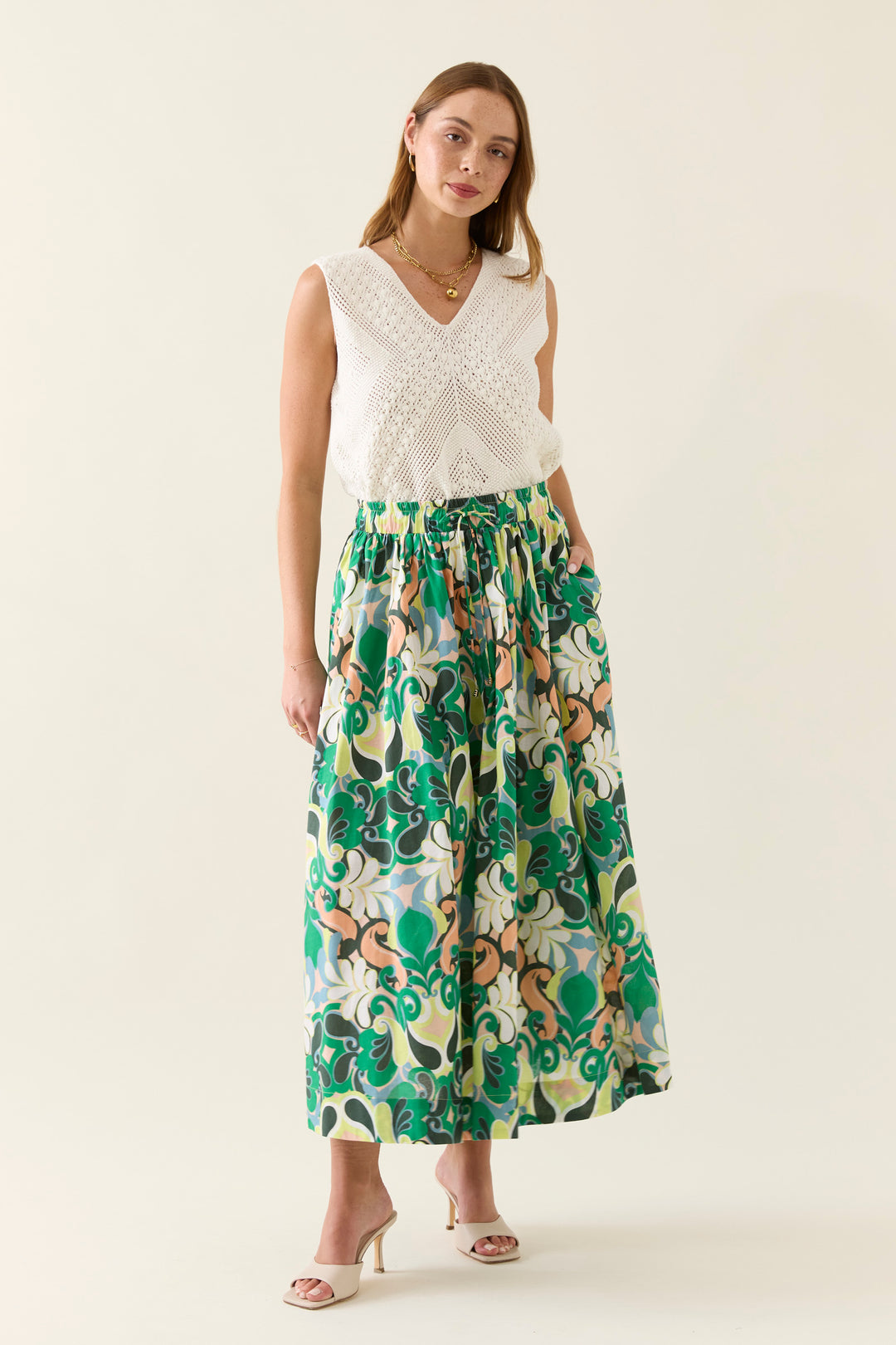 Woman wearing a white sleeveless top and a colorful patterned isle of mine skirt on a beige background
