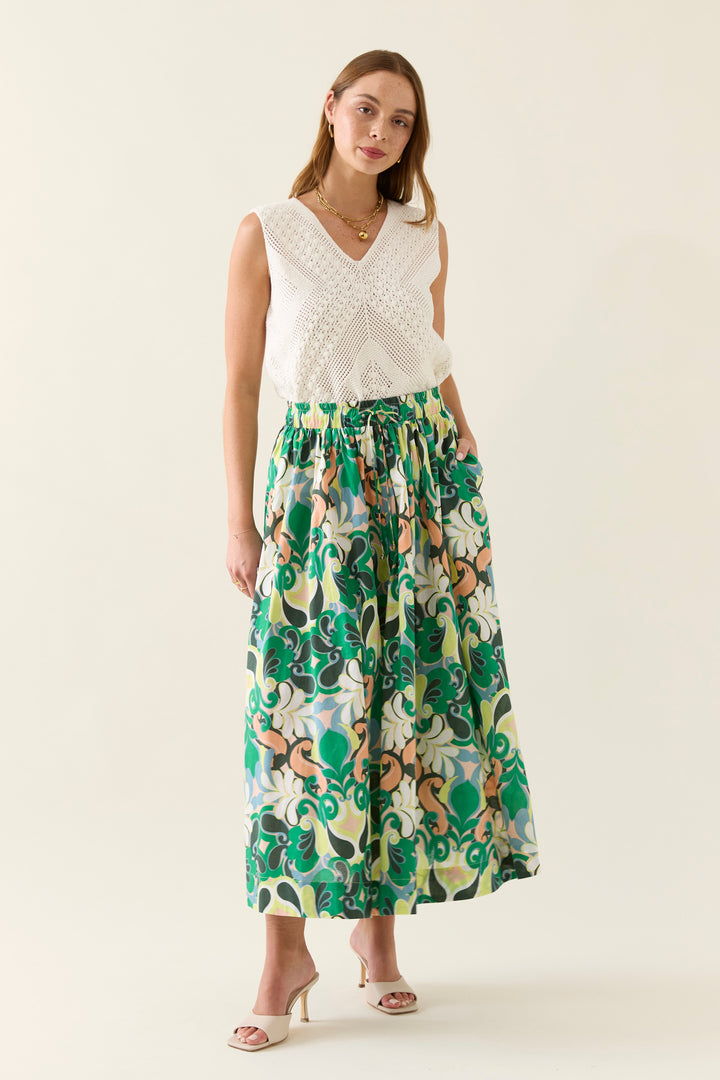 Woman wearing a white sleeveless top and a colorful patterned isle of mine skirt on a beige background