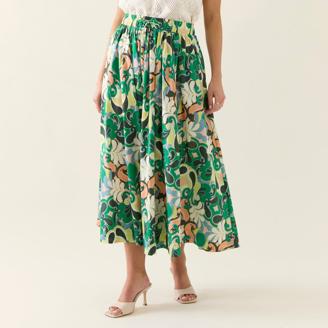 Woman wearing a white sleeveless top and green patterned skirt on a plain background