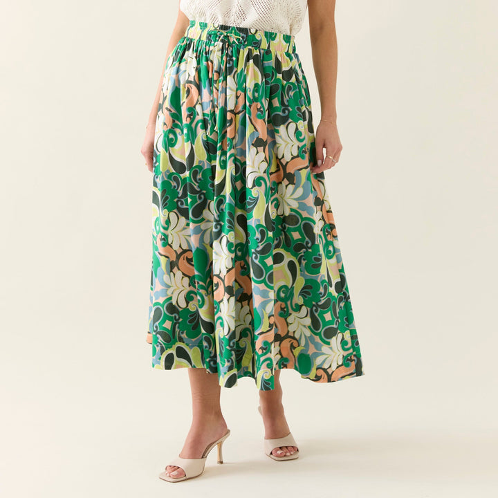 Woman wearing a white sleeveless top and green patterned skirt on a plain background
