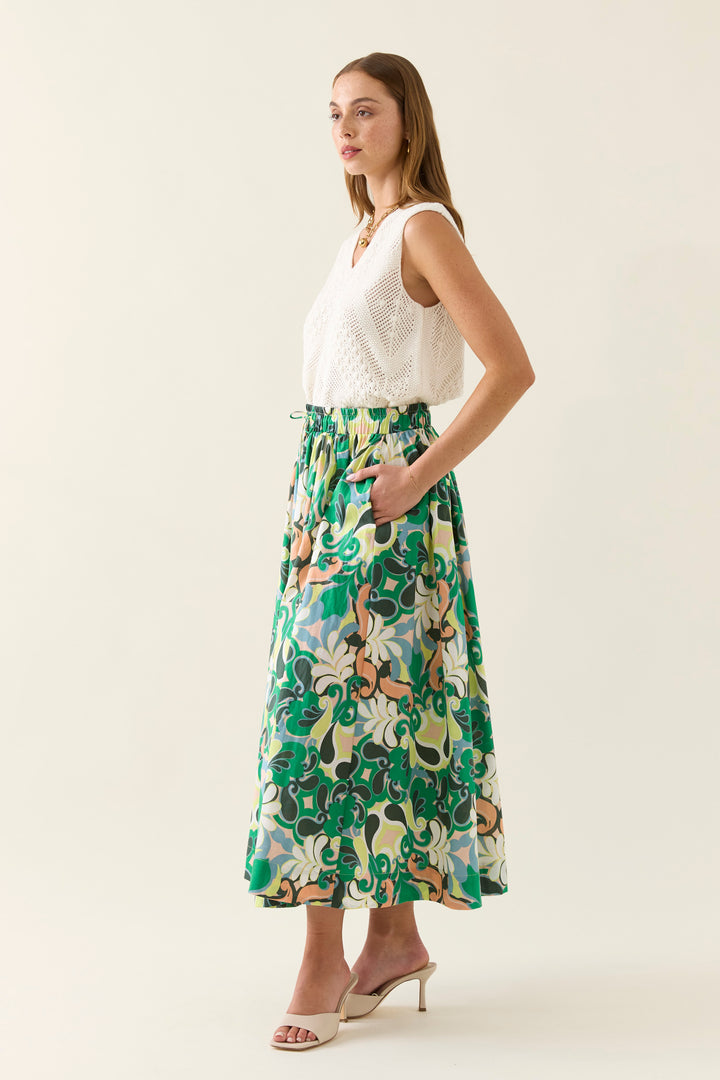 Woman wearing a white sleeveless top and floral isle of mine skirt on a plain background