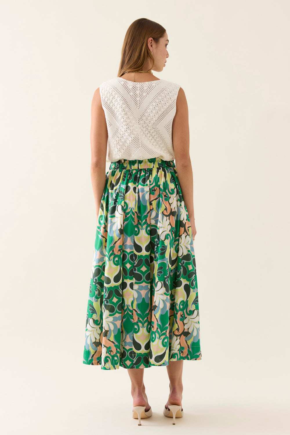 Woman wearing a white sleeveless top and a isle of mine green floral skirt on a white background