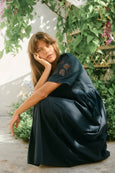 Woman in a navy isle of mine dress sitting outdoors with greenery around