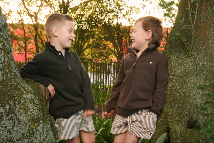 Two children in matching jackets standing on a wooden fence with trees in the background