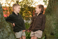 Two children in matching jackets standing on a wooden fence with trees in the background