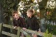 Two children in matching jackets standing on a wooden fence with trees in the background