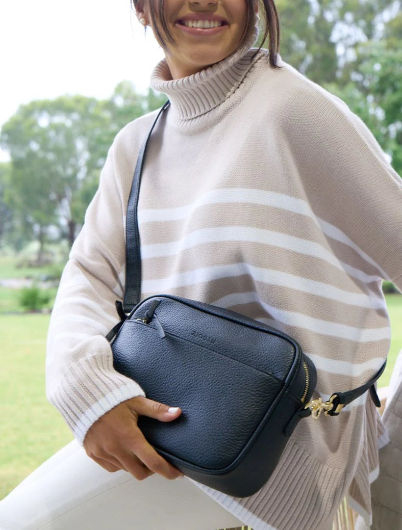 Person wearing a beige poncho holding a black handbag outdoors.