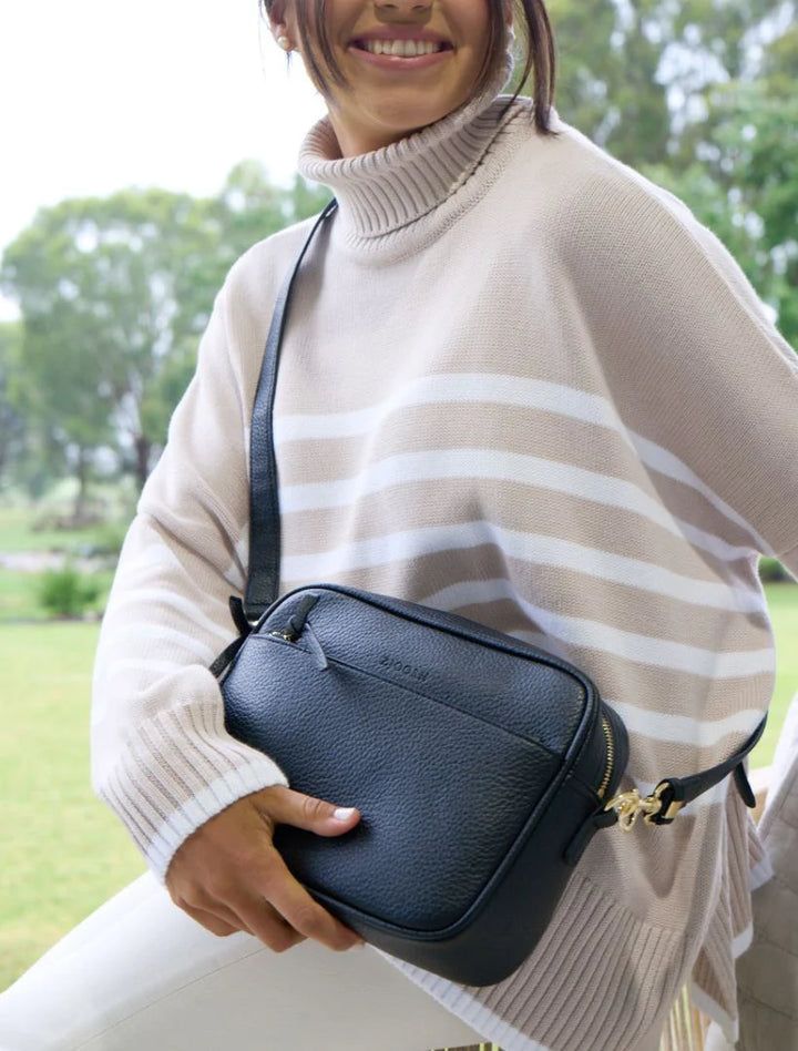 Person wearing a beige poncho holding a black handbag outdoors.
