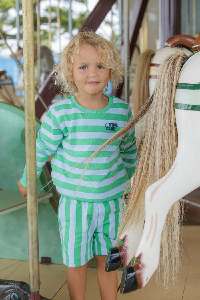 Child in a green and white striped outfit standing next to a carousel horse.