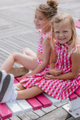 Two young girls in pink checkered dresses sitting on a bench.