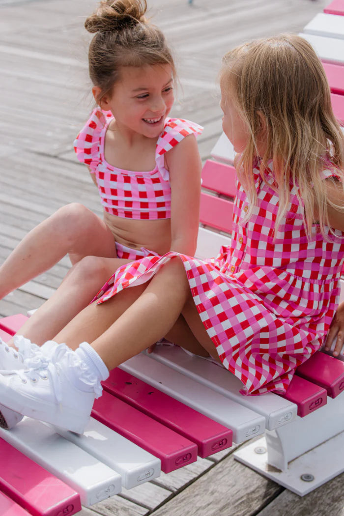 Two young girls in matching Milky pink checkered outfits sitting on a pink and white bench.