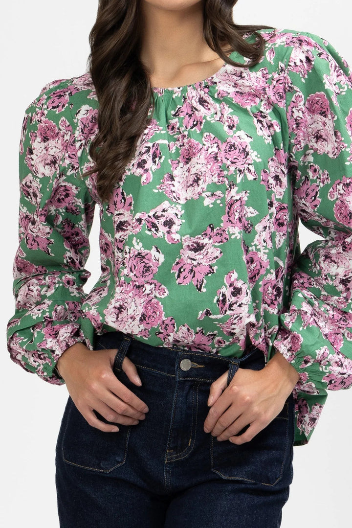 Woman wearing a floral milly blouse with green and pink flowers on a white background
