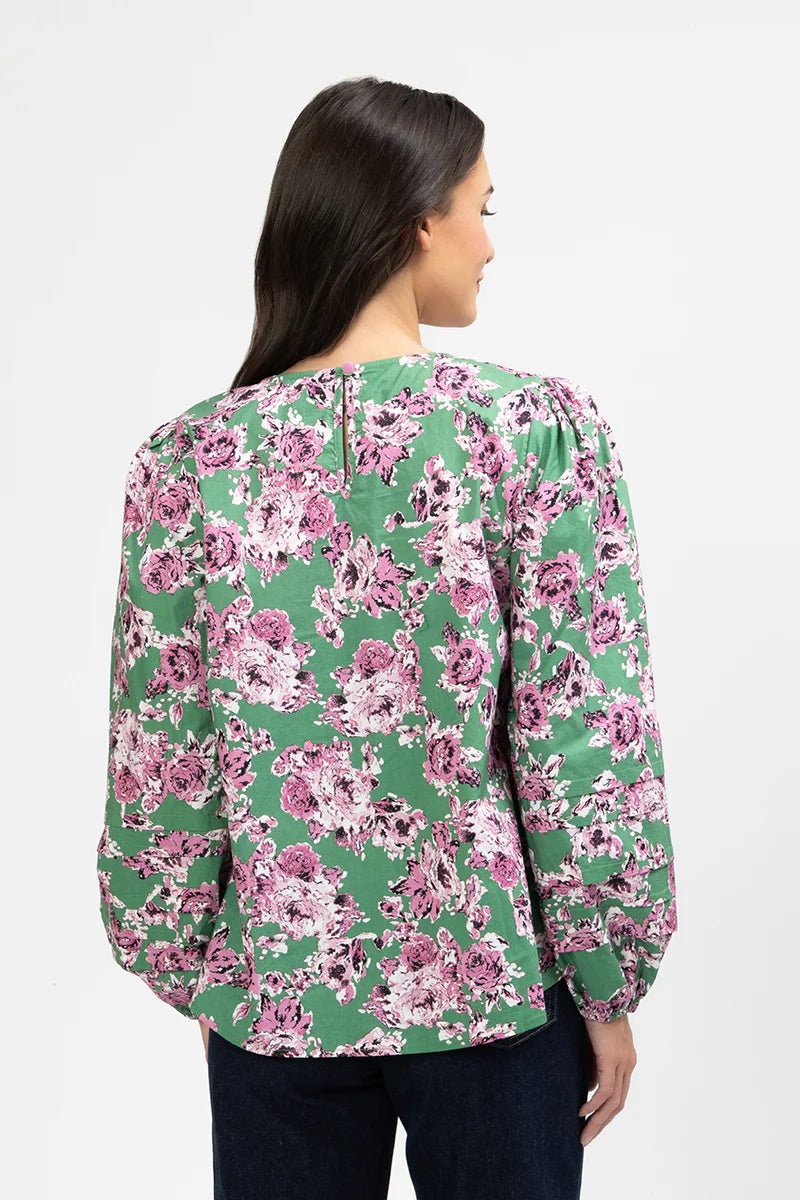 Woman wearing a floral Milly blouse with pink and green flowers on a white background