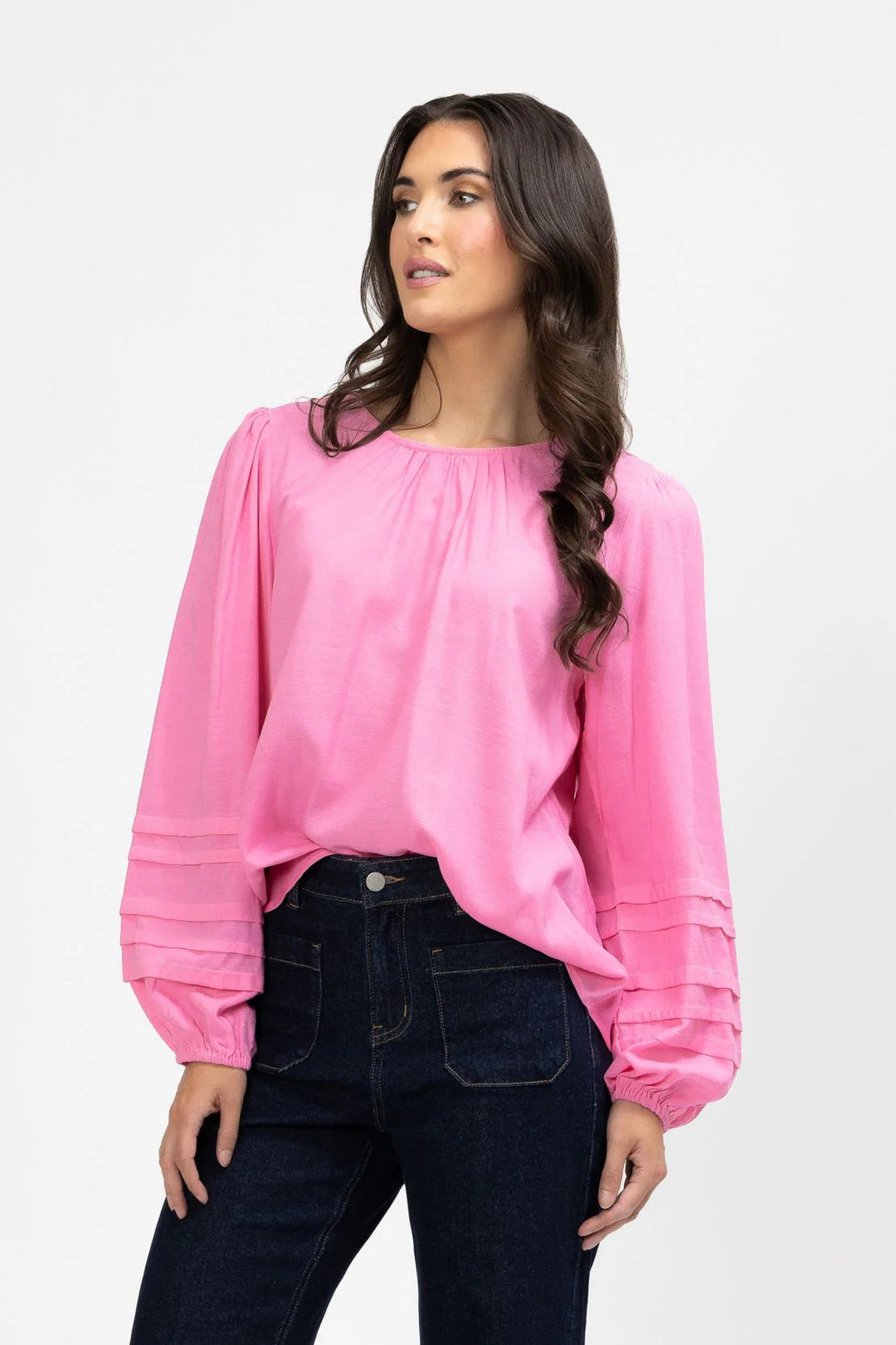 Woman wearing a pink milly blouse and dark jeans on a white background