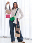 Woman holding multiple colorful handbags against a white curtain background
