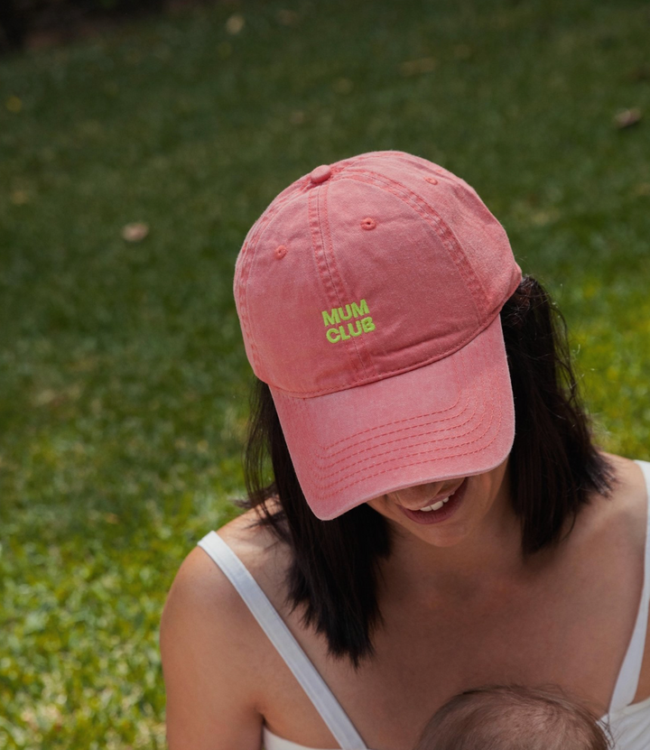 Person wearing a pink cap with 'Mum Club' text, standing outdoors on grass.