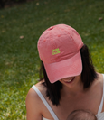 Person wearing a pink cap with 'Mum Club' text, standing outdoors on grass.