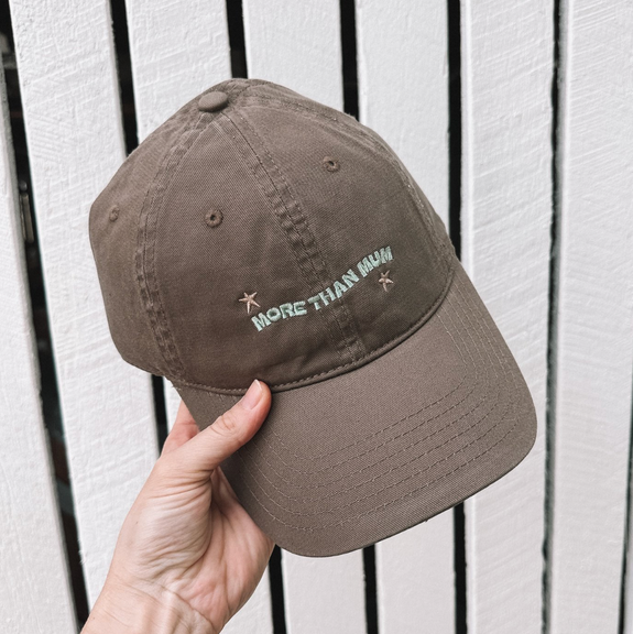Brown cap with embroidered text held against a white background