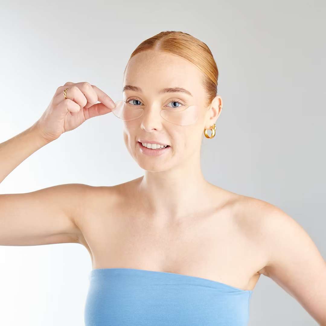 Woman applying clear patches under her eyes on a plain background