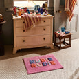 Wooden dresser with a pink rug featuring colorful letters on a tiled floor.