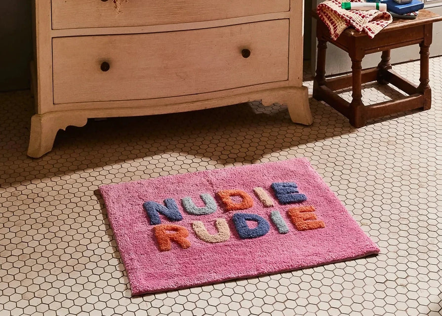 Wooden dresser with a pink rug featuring colorful letters on a tiled floor.