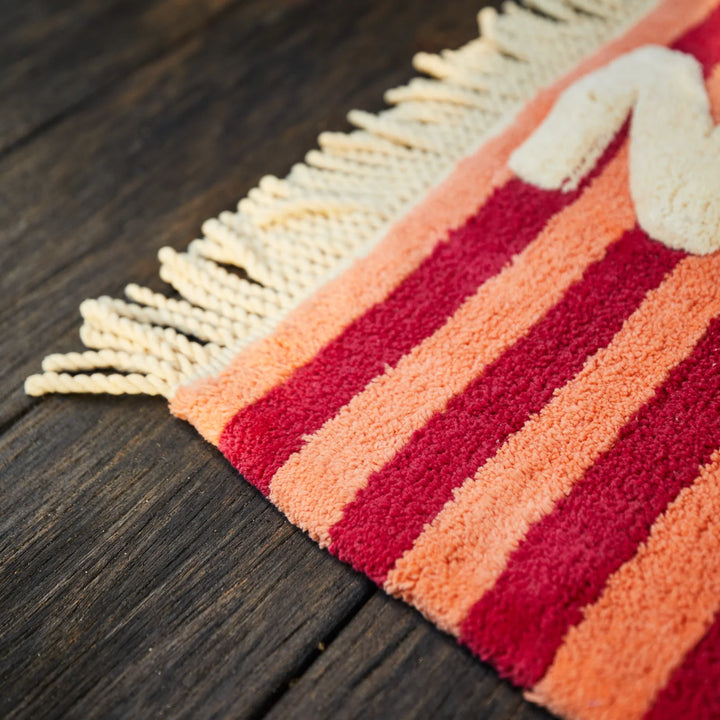 Close-up of a red and orange striped rug with fringes on a wooden floor.