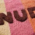 Textured surface with 'Nude' in brown letters on a multicolored background