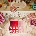 Bathroom with a colorful bath mat displaying 'NUDIE RUDIE' on a marble floor.