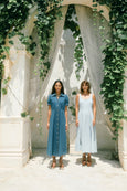 Two women standing under a decorative arch with greenery and white curtains.