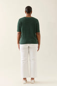 Person wearing a green isle of mine top and white pants on a plain background