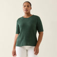 Woman wearing a green isle of mine tee and white pants against a plain background