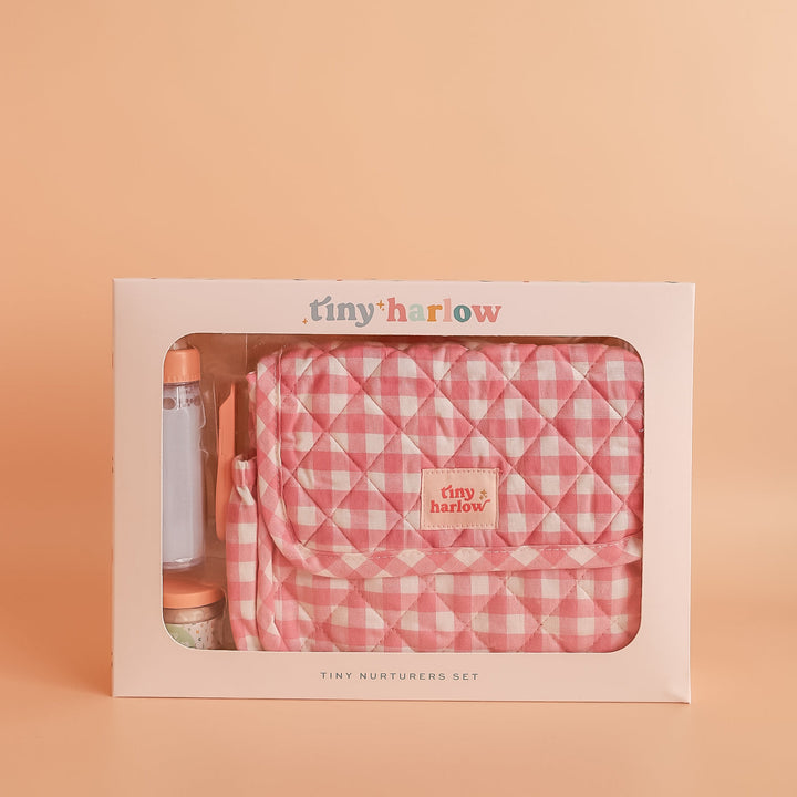 Tiny Harlow Pink checkered dolls bag with baby care items on a beige background