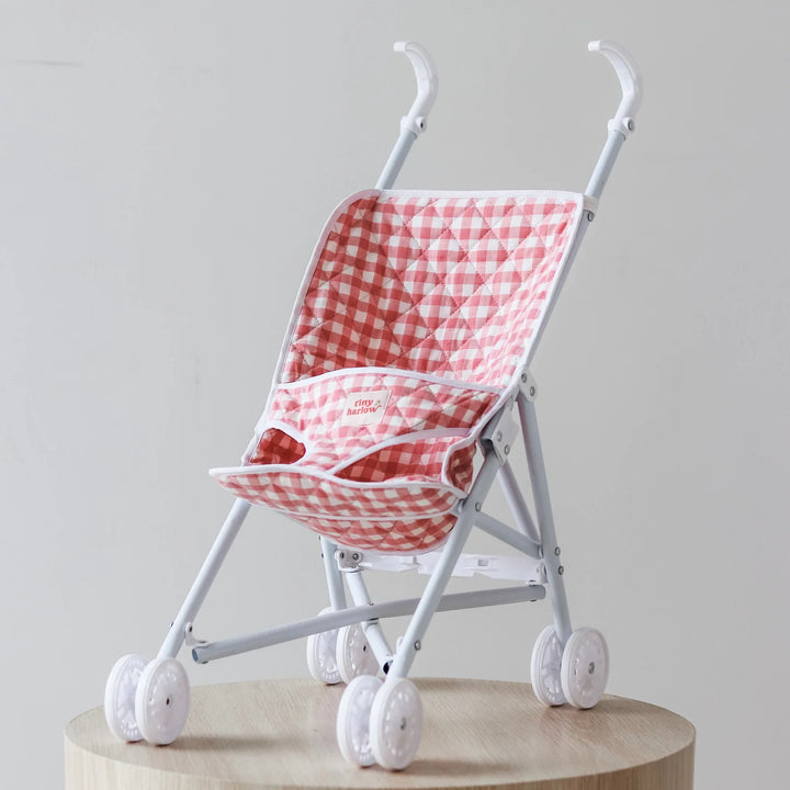 Tiny Harlow red and white gingham dolls stroller on a wooden platform against a light gray background