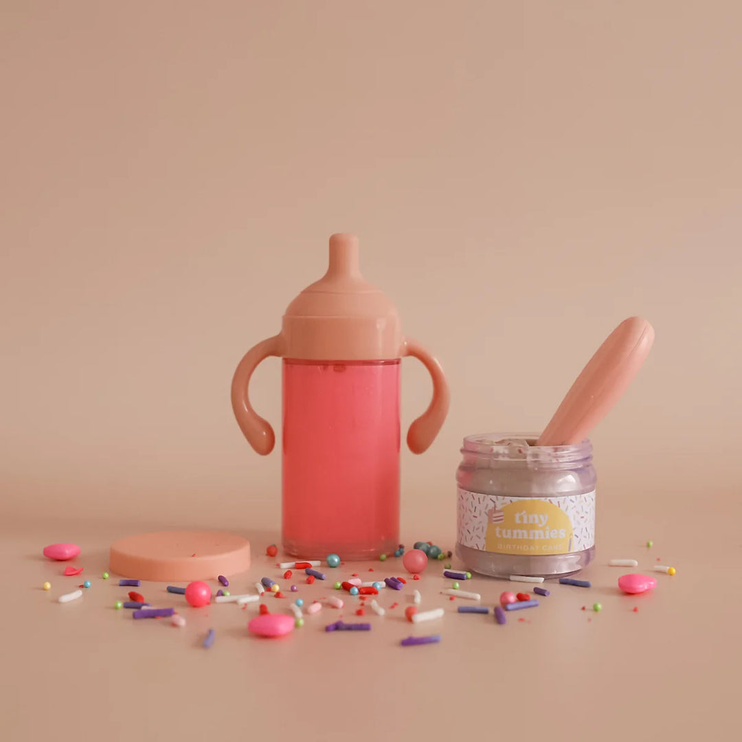dolls Pink sippy cup, jar with spoon, and colorful sprinkles on a beige background