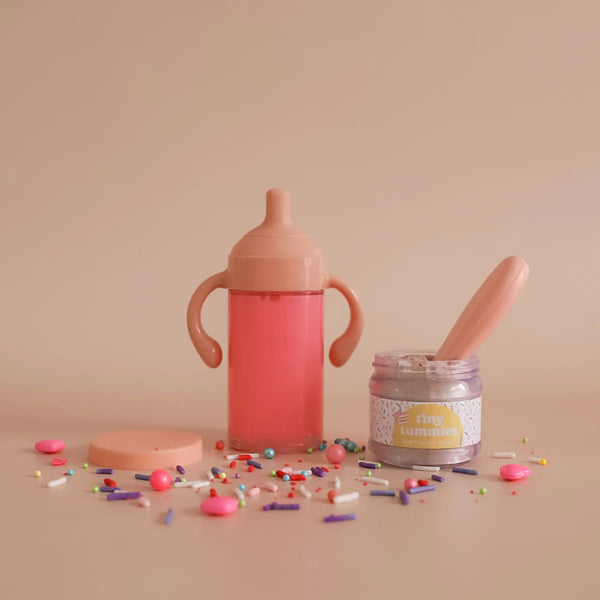 dolls Pink sippy cup, jar with spoon, and colorful sprinkles on a beige background